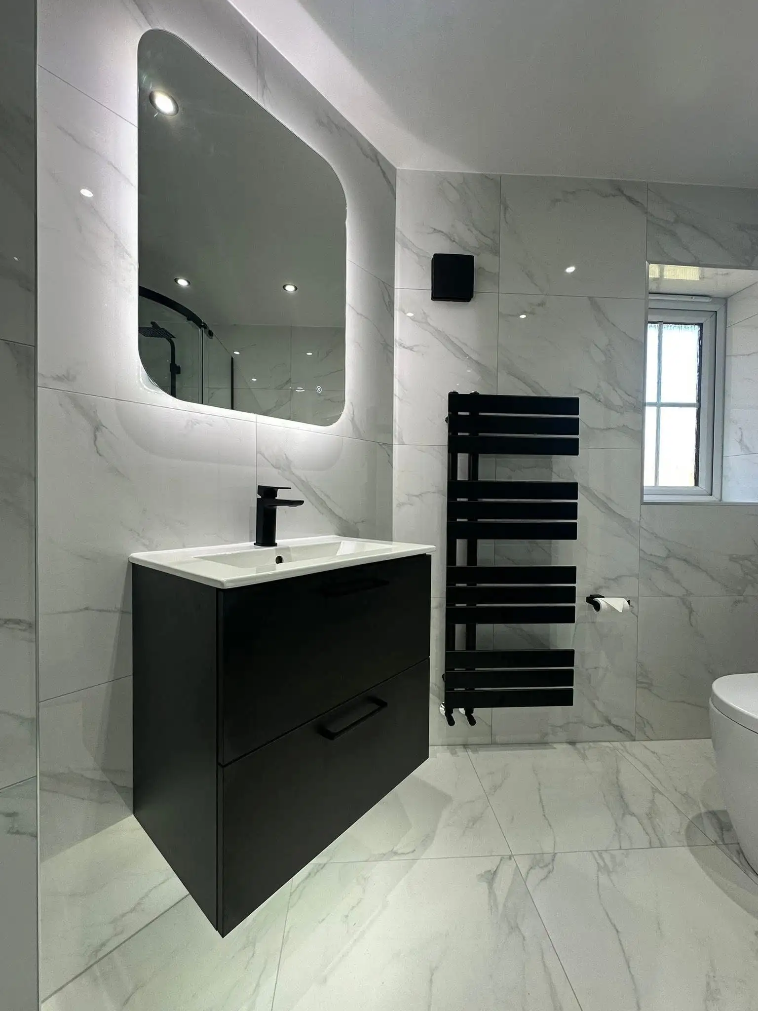 Luxury bathroom with marble-effect wall and floor tiles, matte black vanity unit and backlit LED mirror