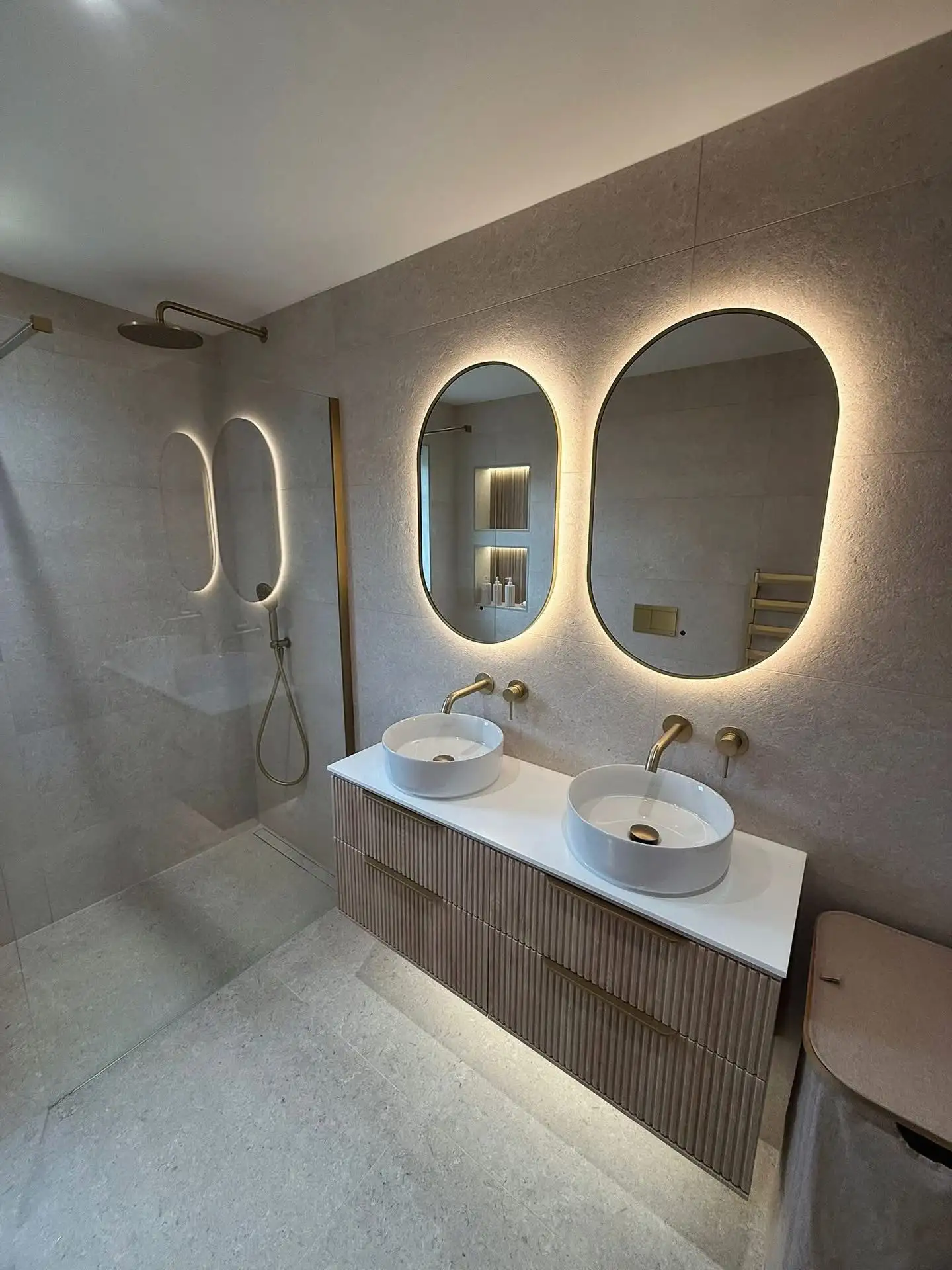 Modern bathroom with warm stone-effect tiles, walk-in shower with ceiling rainfall head, fluted timber double vanity and round vessel basins